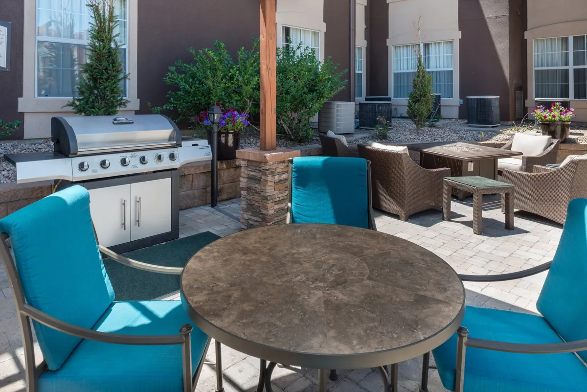 An inviting outdoor space featuring a stone table and comfortable seating arranged around an outdoor grill, set within the hotel’s landscaped grounds. The area is designed for socializing, casual meetings, or unwinding after work, with a relaxed, friendly atmosphere that encourages connection.