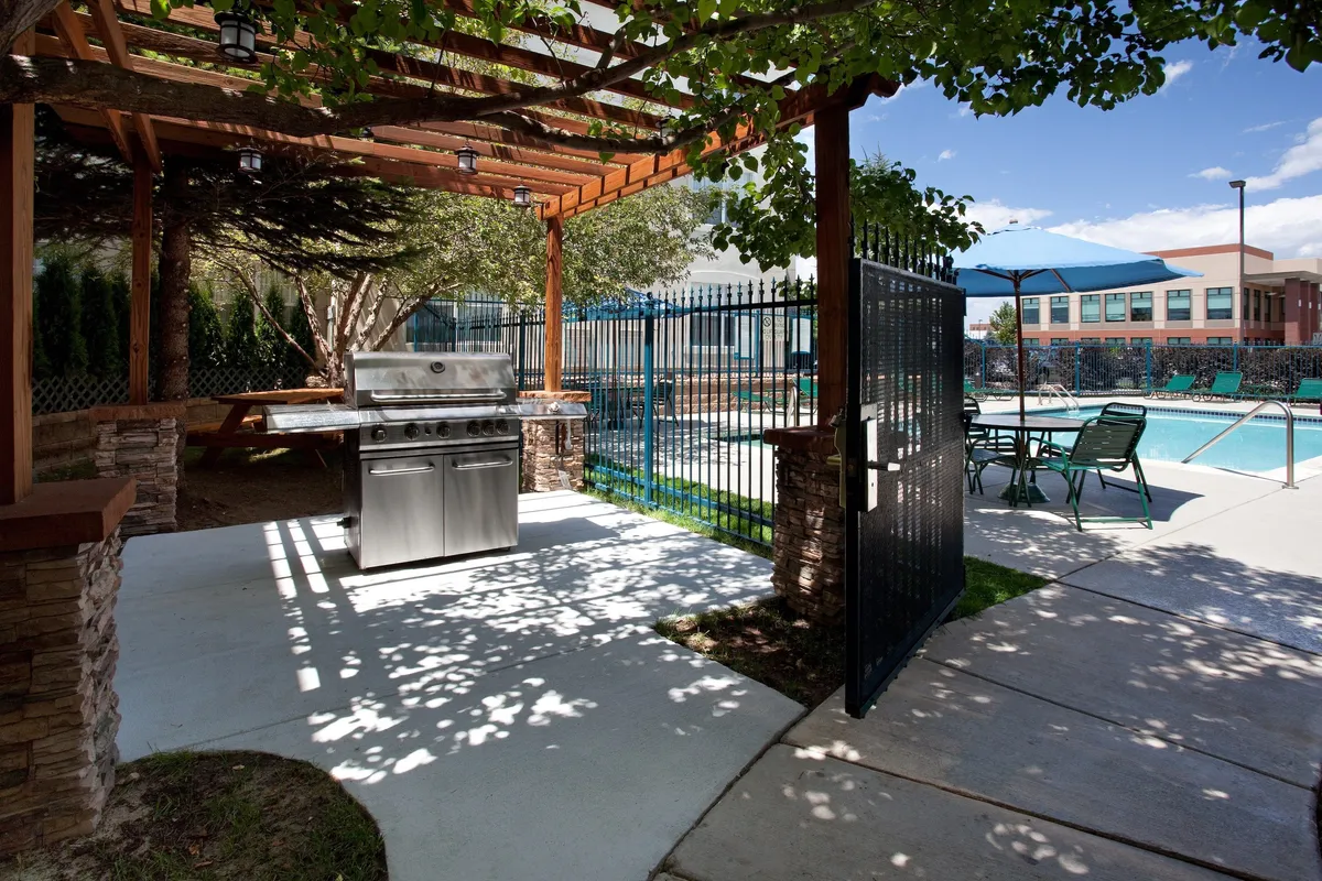 A vibrant outdoor scene featuring a swimming pool, a grill setup, a pergola, and multiple lounge chairs. The area is designed for both relaxation and social gatherings, with plenty of space for guests to swim, barbecue, or simply soak up the sun. The mood is lively yet relaxed, ideal for both families and groups of friends.