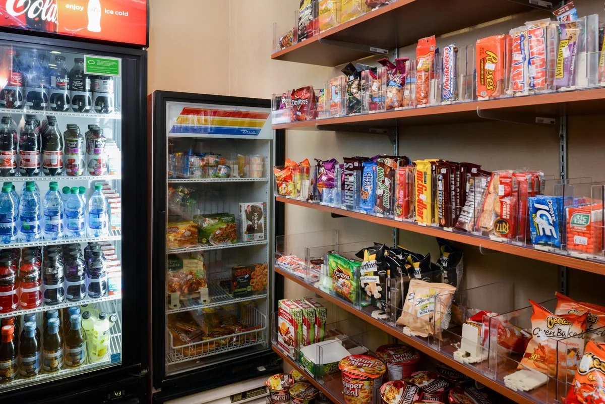 A contemporary snack and beverage area with shelves stocked full of snacks, a cold food display, and a beverage refrigerator—perfect for grabbing a quick bite or keeping favorite snacks on hand for late-night cravings.