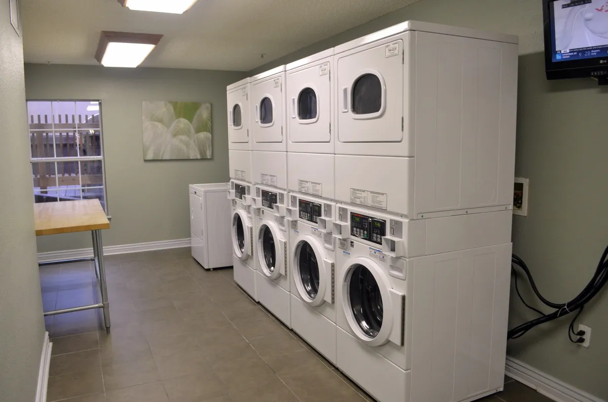 A practical, well-organized laundry room equipped with multiple washing machines, dryers, and a folding table. The inclusion of a TV suggests added comfort, making routine chores more enjoyable for guests staying longer.