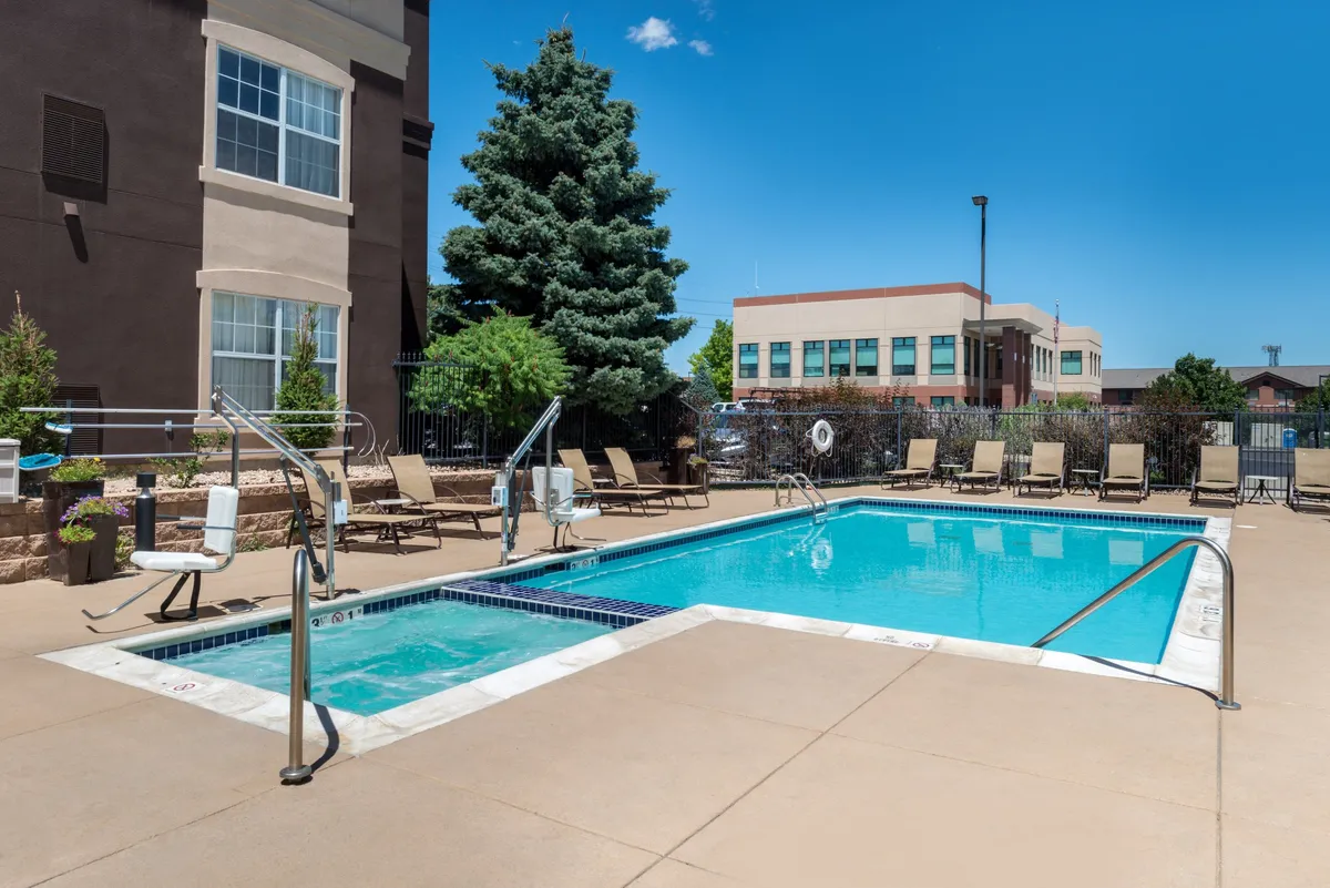 This image features the property's exterior pool area surrounded by lounge chairs and lush landscaping. The scene captures a tranquil, sunlit space ideal for relaxation, socializing, or unwinding after a busy day. The inviting water and poolside seating evoke a leisurely, comfortable atmosphere.